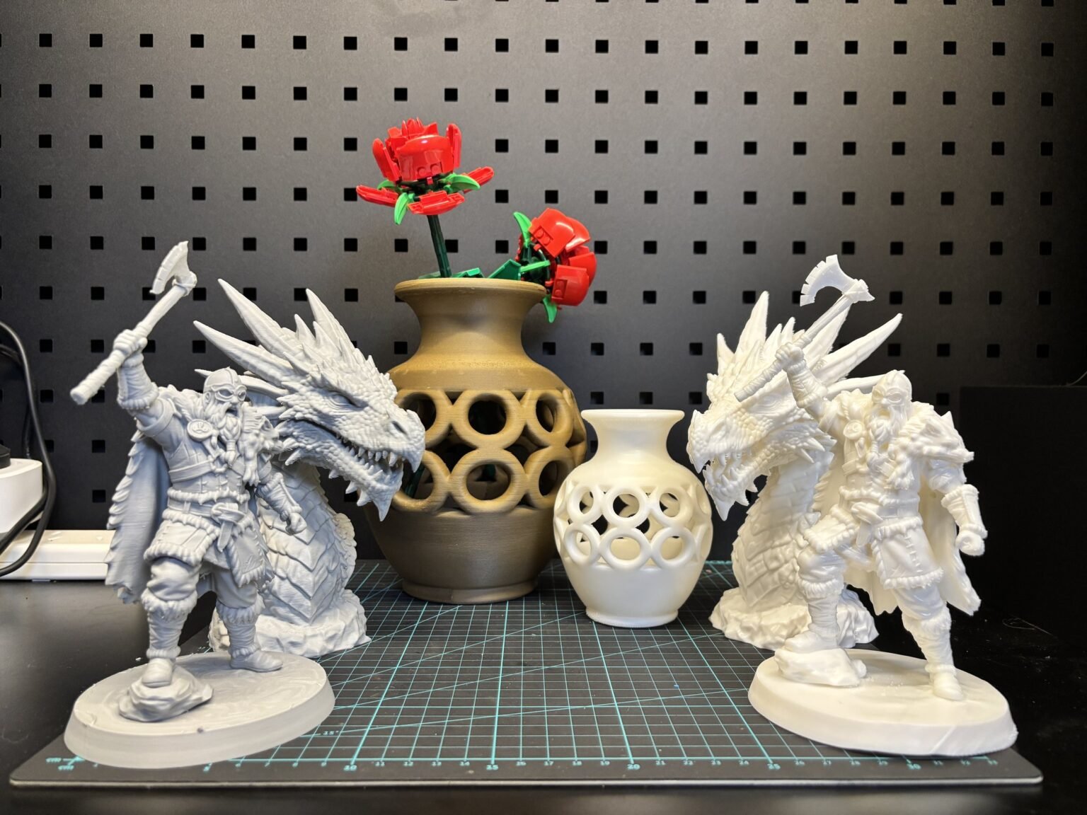 Two 3D printed fantasy warrior and dragon figures, FDM on the left and resin on the right, beside two 3D printed lattice vases holding LEGO roses