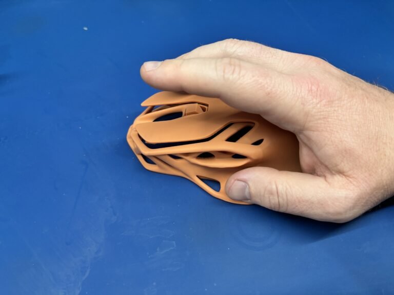 Hand resting on an orange 3D printed computer mouse shell