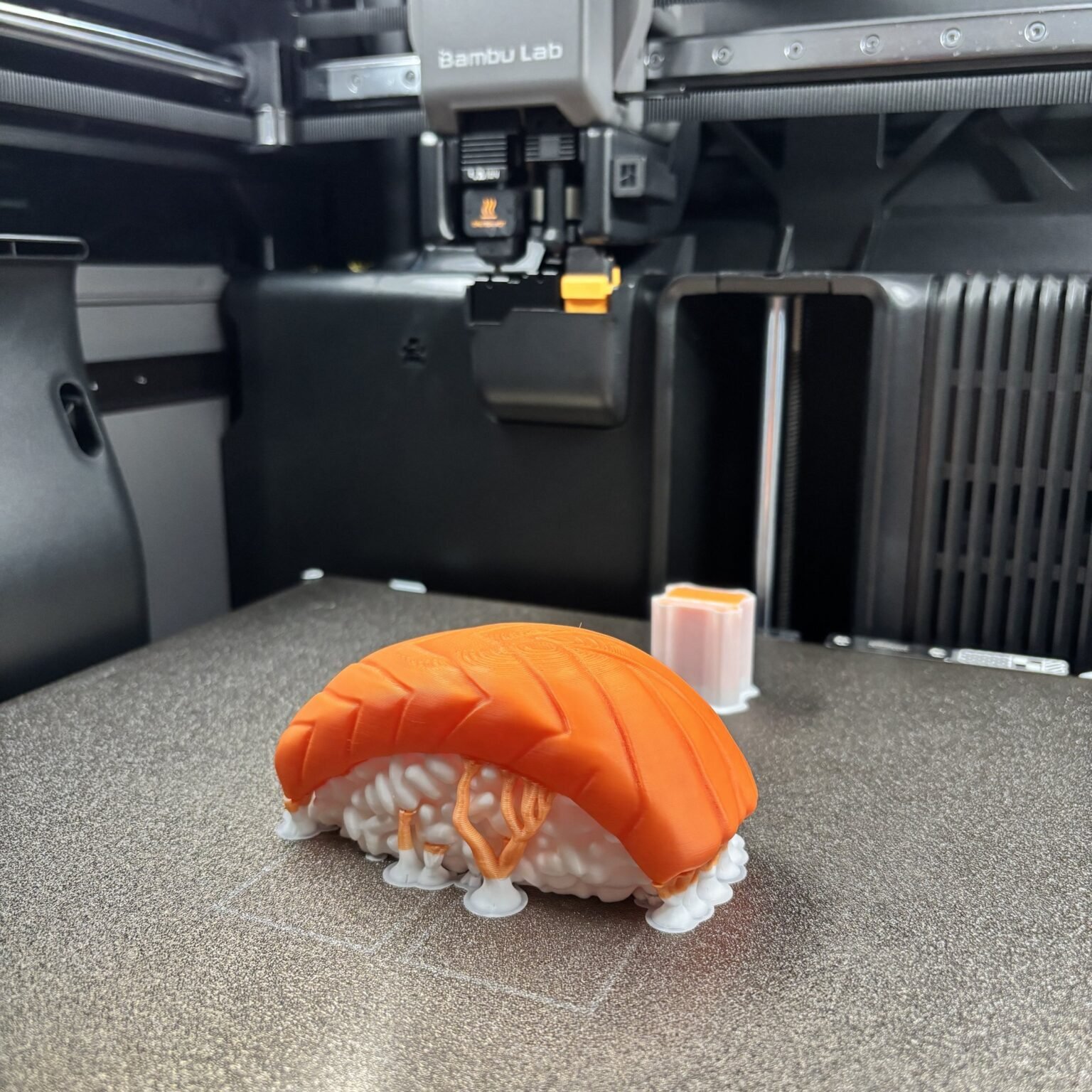 Multi-colour 3D printed salmon nigiri in orange and white on a printer build plate