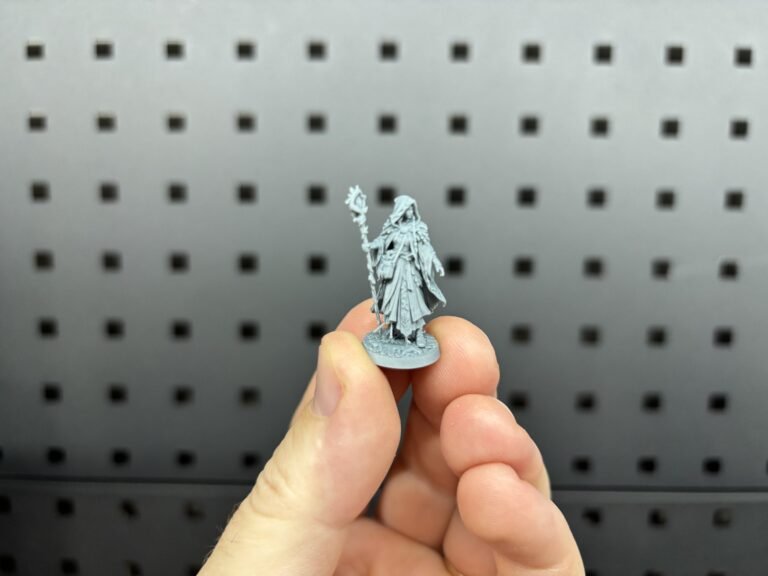 Small grey resin 3D printed druid miniature held between finger and thumb